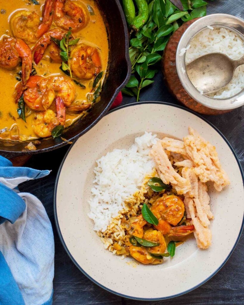 Kerala Shrimp Curry in a black cast iron pan with curry leaves and rice.Also in a white plate with rice.