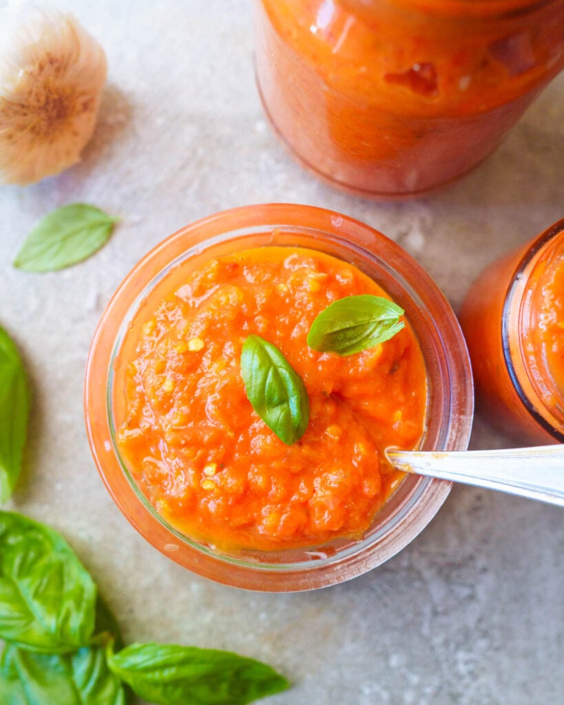 Roasted Tomato & Red Peppers Pasta Sauce in jars with fresh basil leaves on top of it