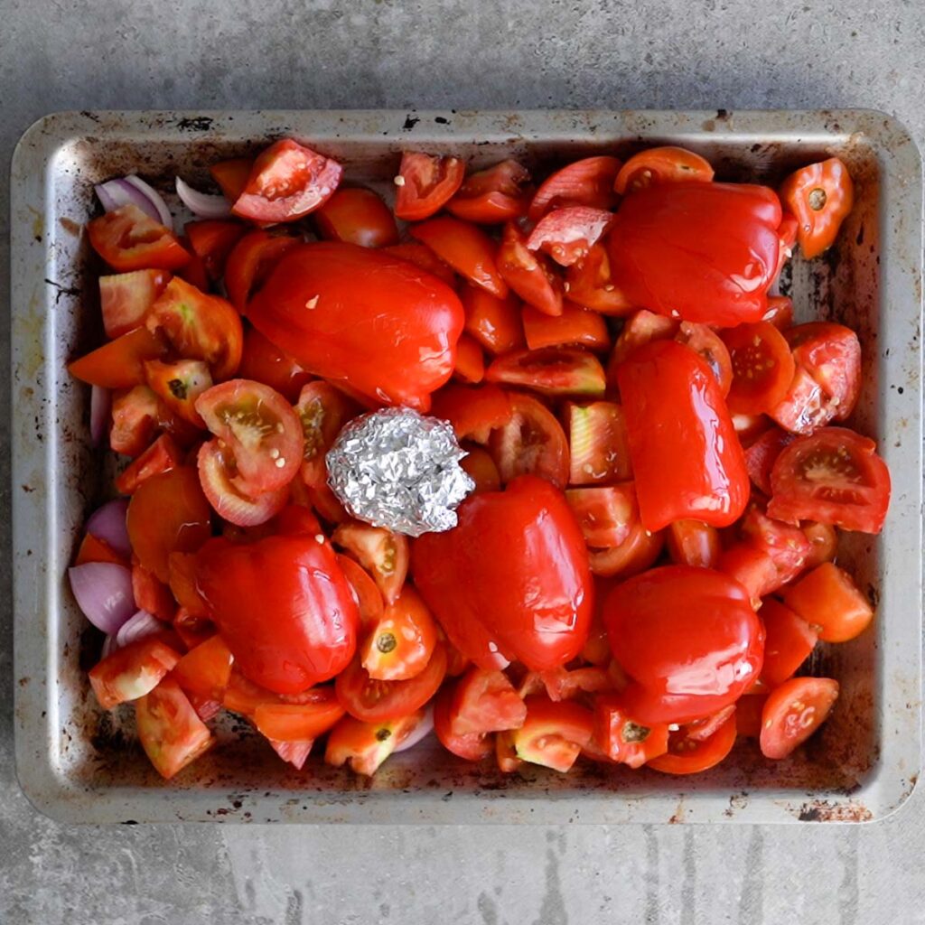 Garlic wrapped in foil,Tomatoes, red peppers and onions on a baking tray