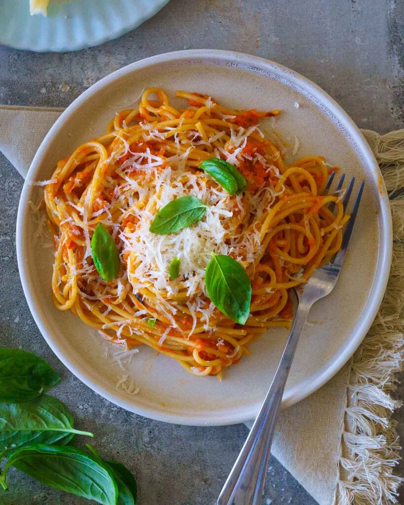 Spaghetti tossed with roasted tomato sauce on a white plate with parmesan and basil 