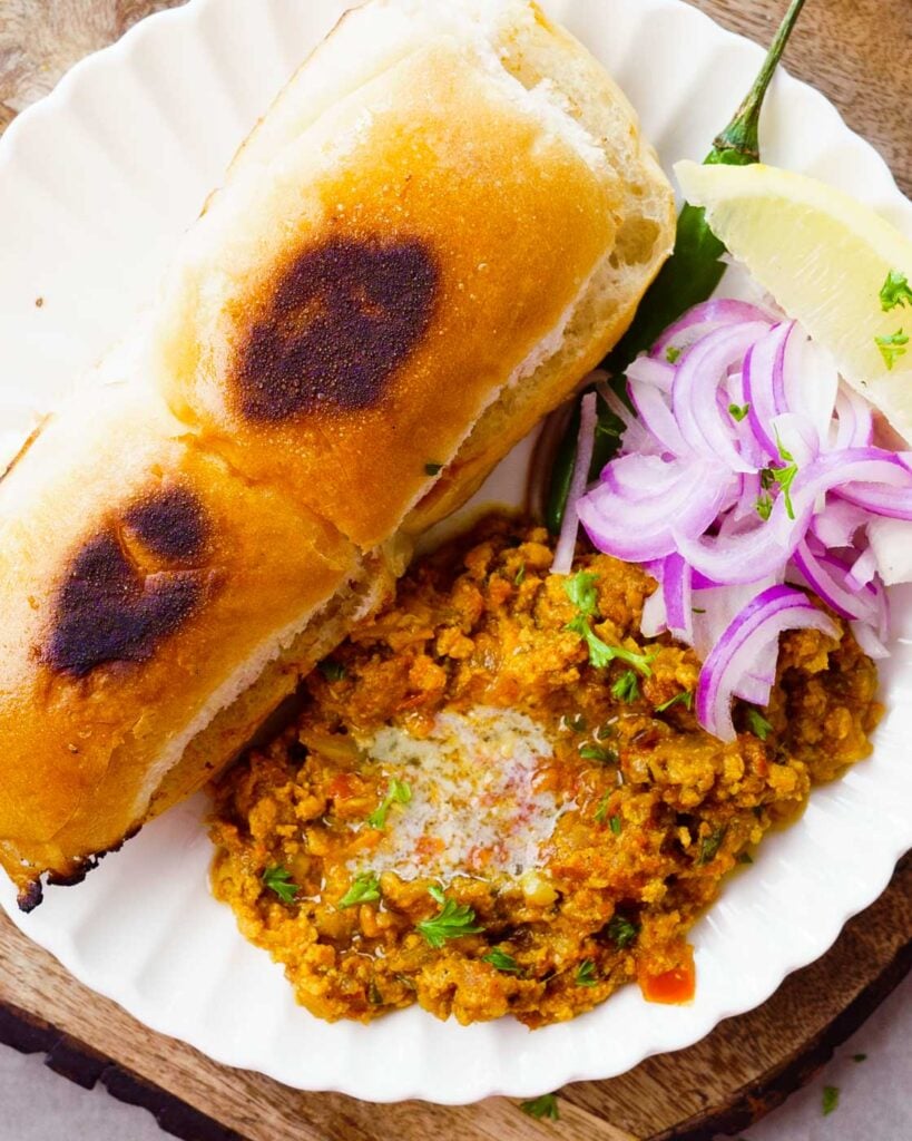 Chicken Keema with butter, onions and toasted pavs on top of a white plate