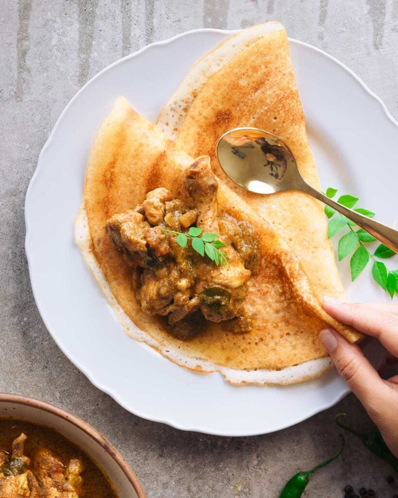 Pepper chicken curry on top of dosas with curry leaves.