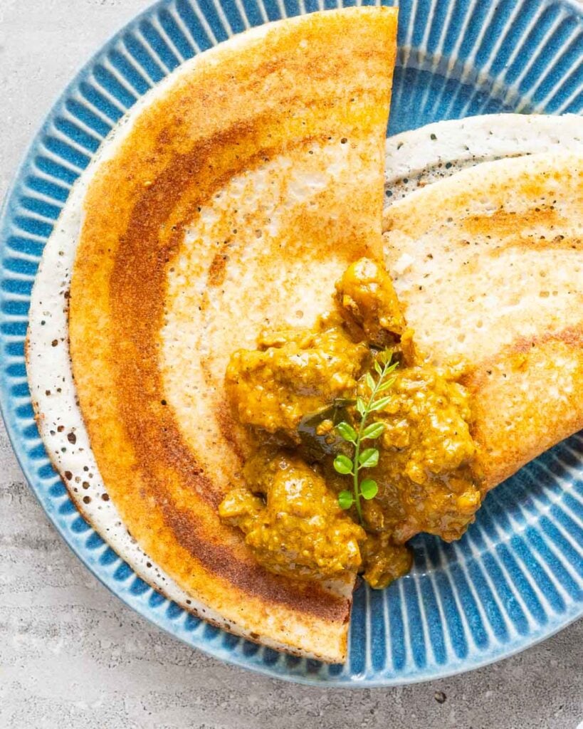 kerala coconut curry on top of two dosas in a blue plate with a garnish of small baby curry leaves