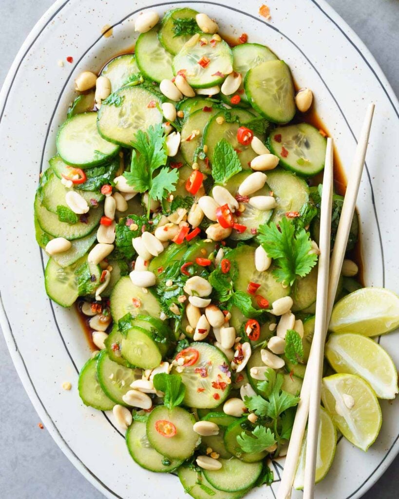 Spicy Asian Cucumber Salad with Peanuts on a long platter, with chop sticks on the side. Garnished with peanuts, bird eye chilies, and cilantro