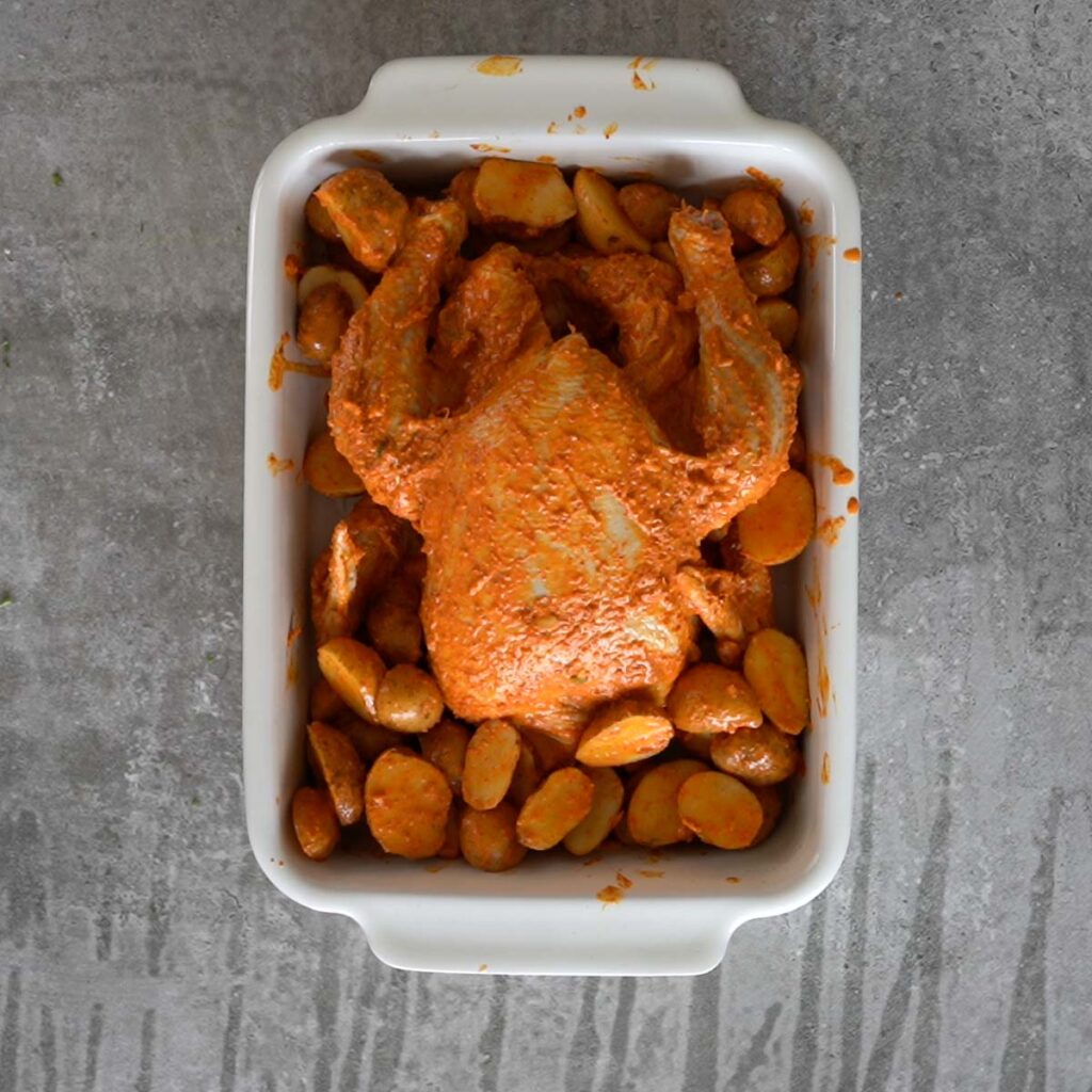 Marinated chicken in a white baking pan with baby potatoes