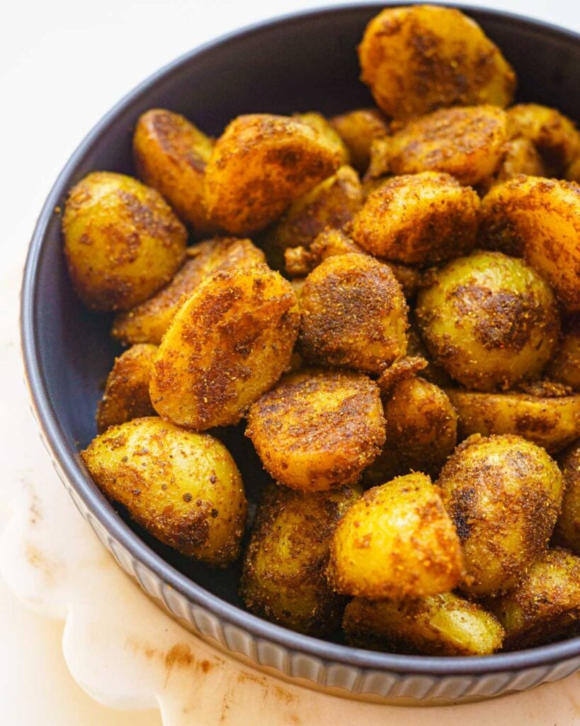 Black shallow bowl with roasted masala baby potatoes in it