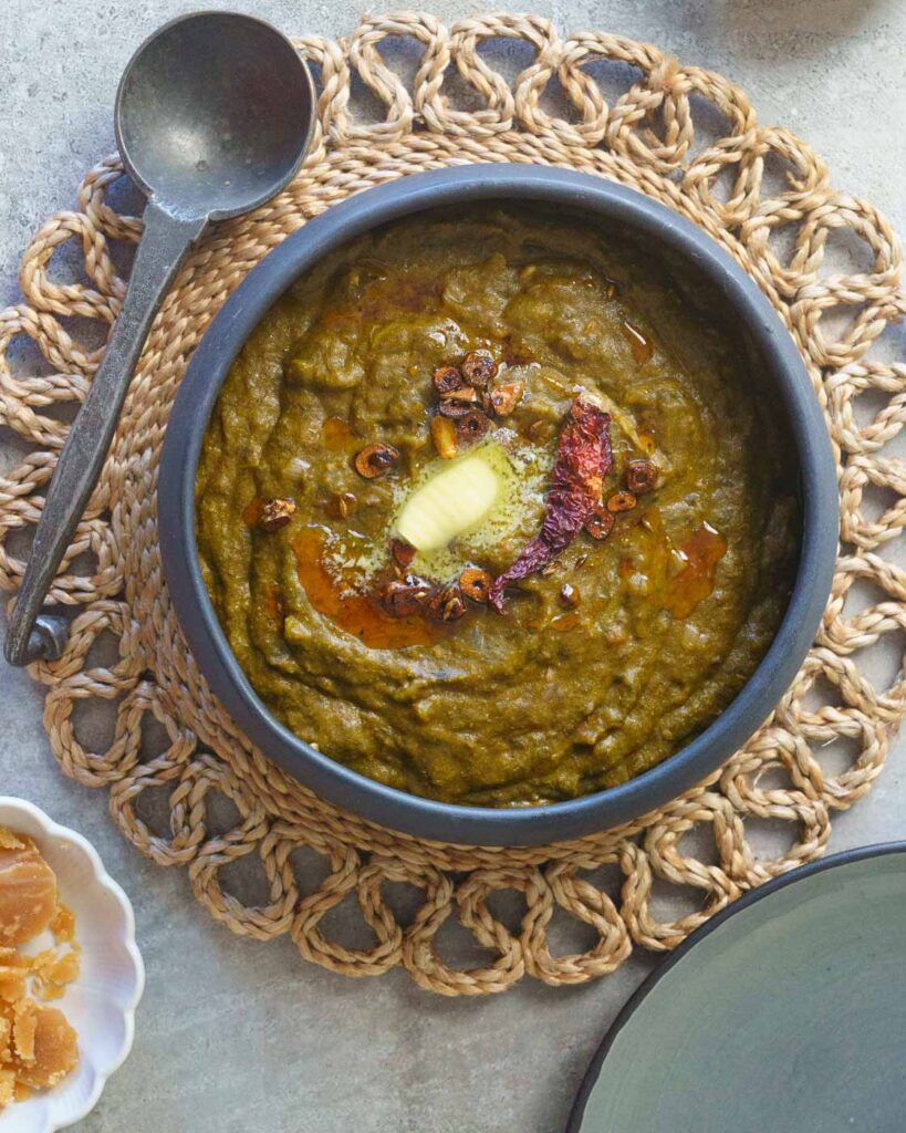 Sarson ka saag in a black bowl with a tempering of garlic, chili and ghee, topped with a knob of butter