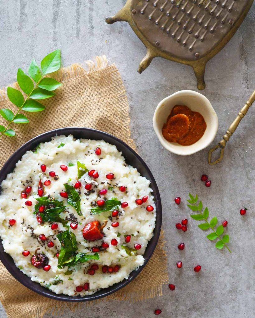 Curd Rice with pomegranate seeds, tempering of mustard seeds, curry leaves and chilies on a grey background , served with lime pickle.
