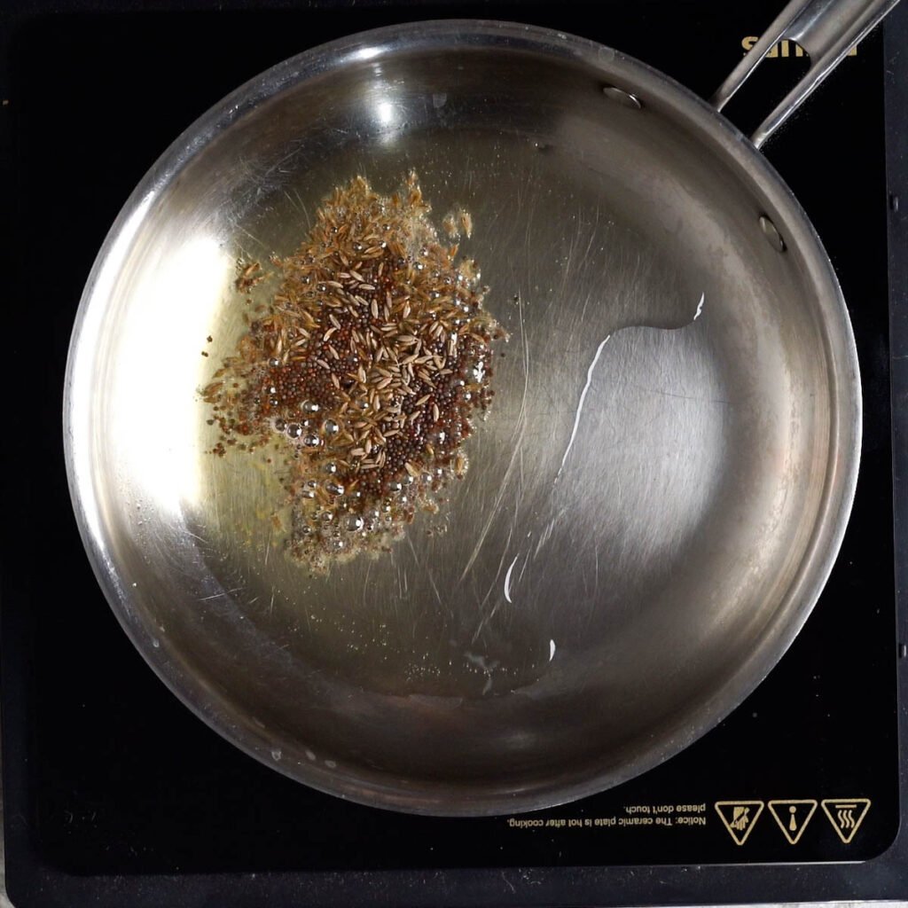 Tempering Cumin and mustard seeds in a steel pan with hot oil