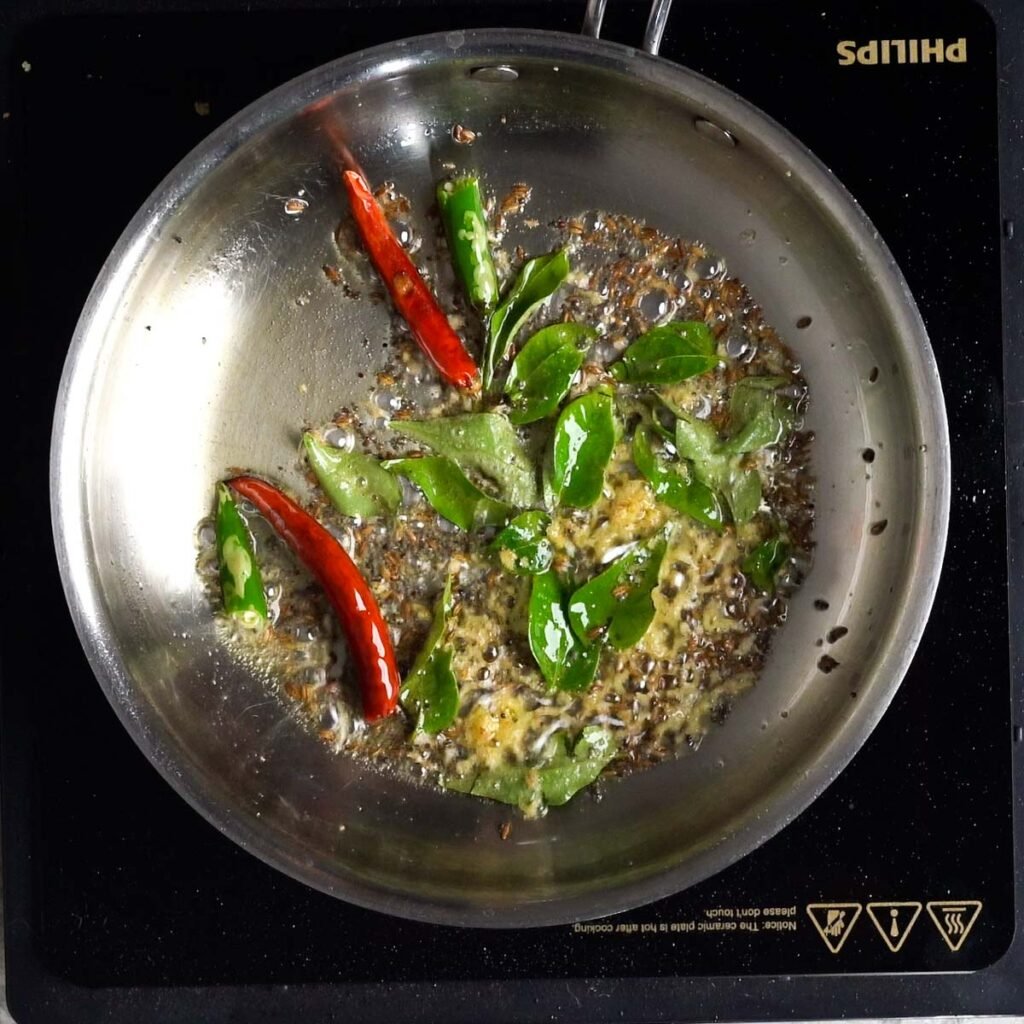 Tempering Cumin, red chilies, curry leaves, ginger and mustard seeds in a steel pan with hot oil