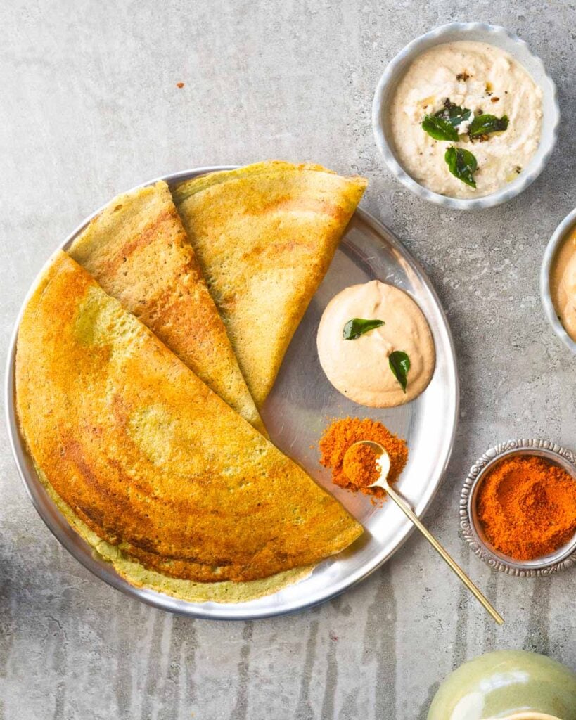 Pesarattu or Green Moong Dosa on a steel plate with peanut chutney and podi