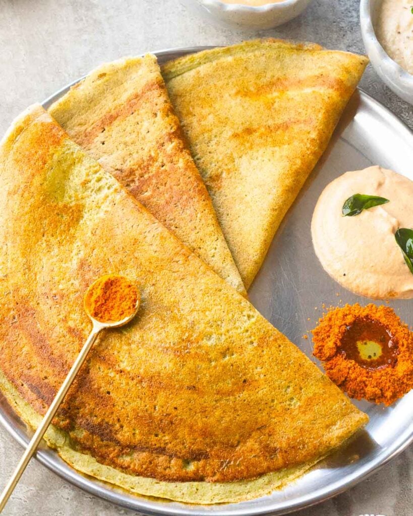 Pesarattu or Green Moong Dosa on a steel plate with peanut chutney and podi