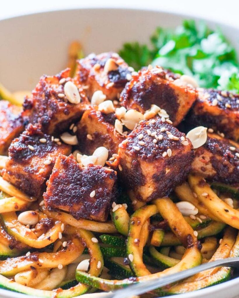 Crispy thai tofu with peanut butter and chili sauce served over zucchini noodles