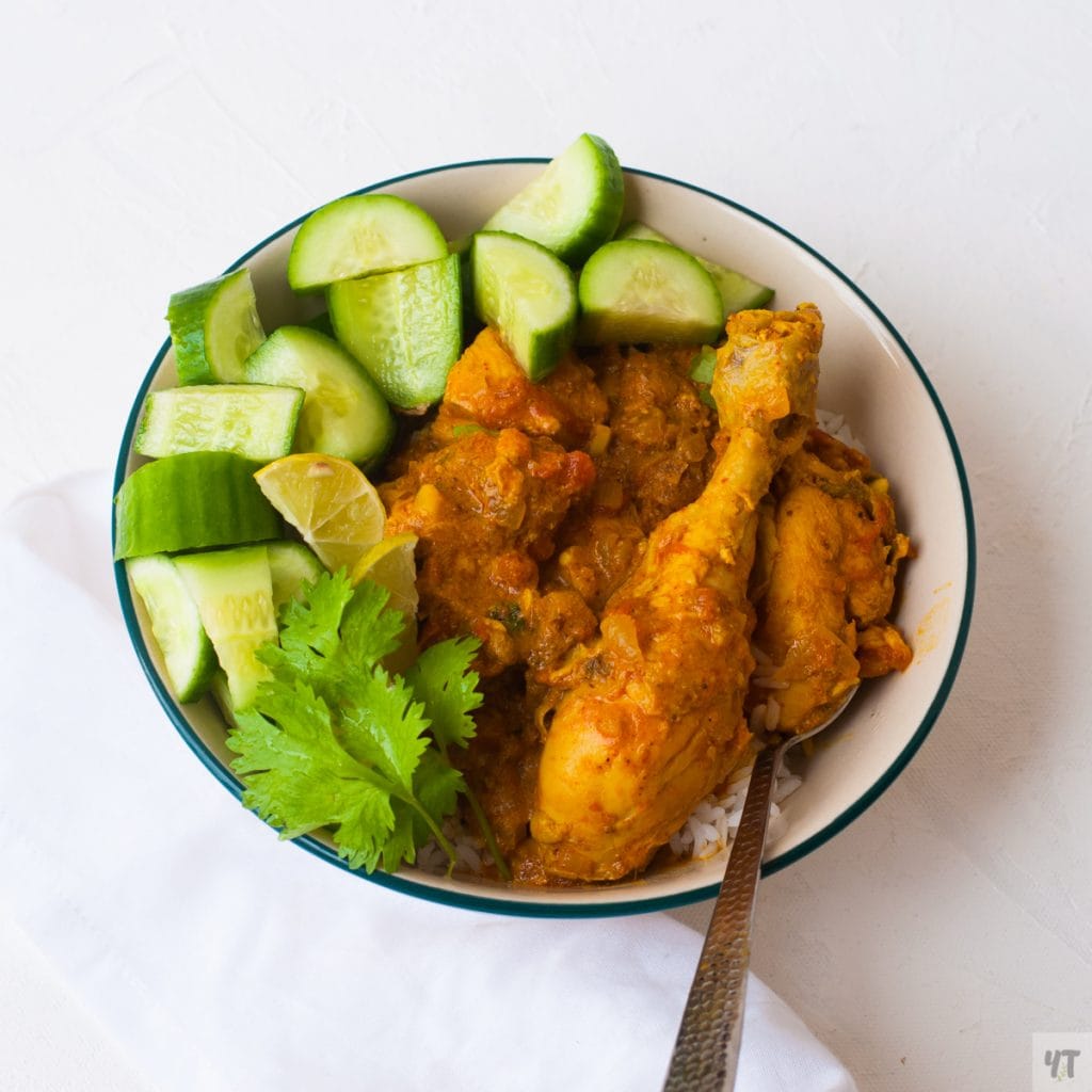 Instant Pot Indian Chicken Curry in a large white bowl on top of white rice and cucumbers