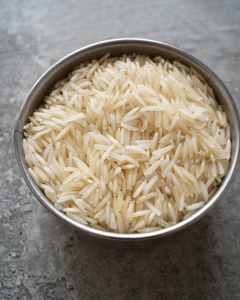 close up of indian basmati rice in a measuring cup on a grey background