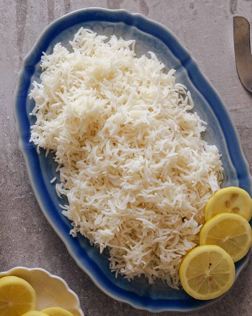 Fluffy white basmati rice or long grain indian rice made in the instant pot in a blue platter with lemon on the side.
