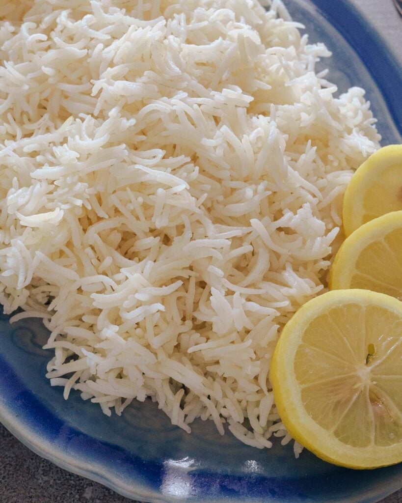 Fluffy white basmati rice or long grain indian rice made in the instant pot in a blue platter with lemon on the side.