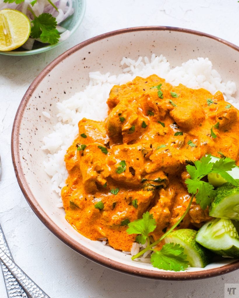 Delicious butter chicken served in a bowl over steaming hot rice &  cucumber salad, garnished with fresh cilantro
