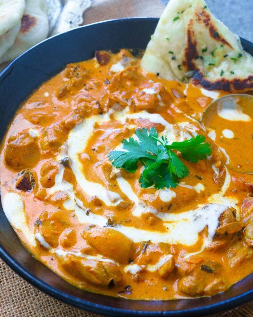 Butter chicken in a black bowl with cilantro and a drizzle of cream