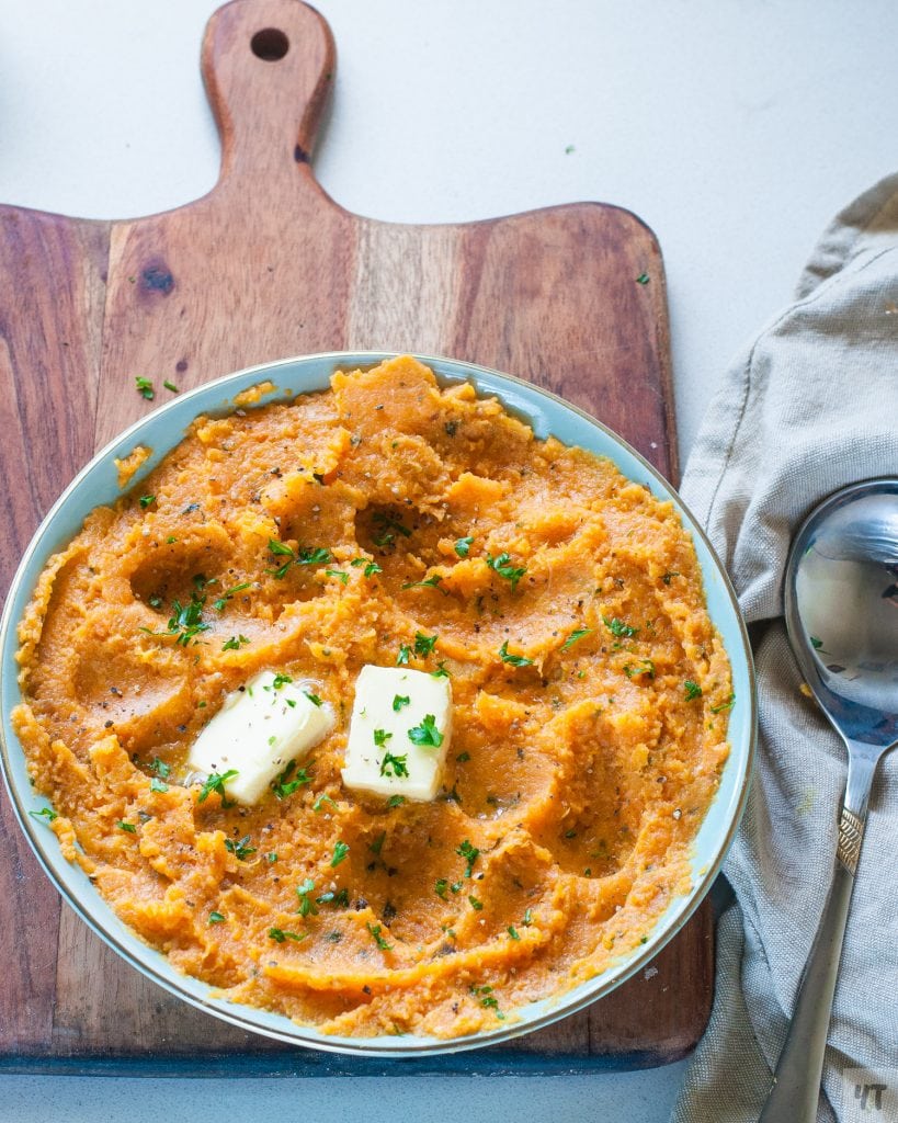 Instant Pot Mashed Sweet Potatoes in a green bowl with butter and parsley