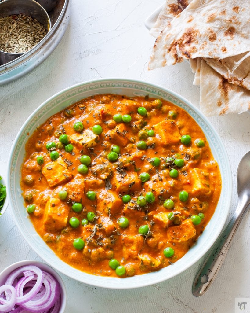 Instant Pot Matar Paneer in a light green shallow bowl with onions,naan and spices