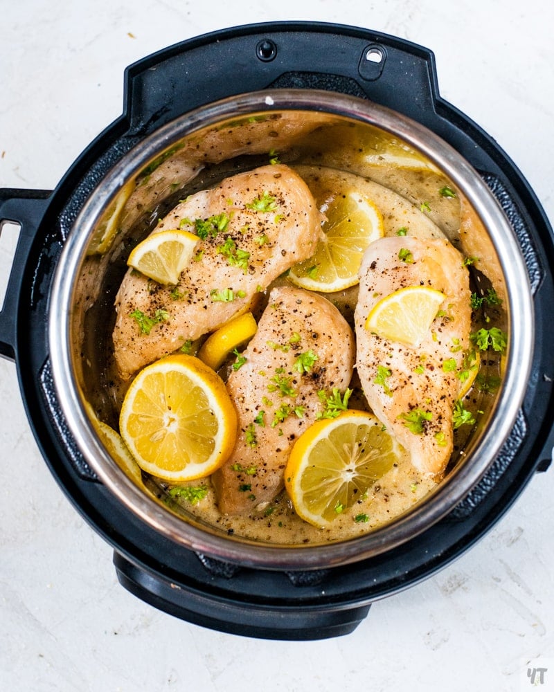 instant pot lemon garlic chicken inside the inner pot with a garnish of lemon slices and parsley