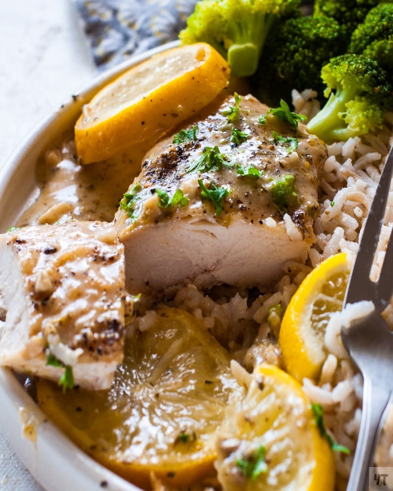 Close up of instant pot lemon garlic chicken on a white plate with a garnish of lemon slices and parsley on a bed of brown rice and steamed brocolli