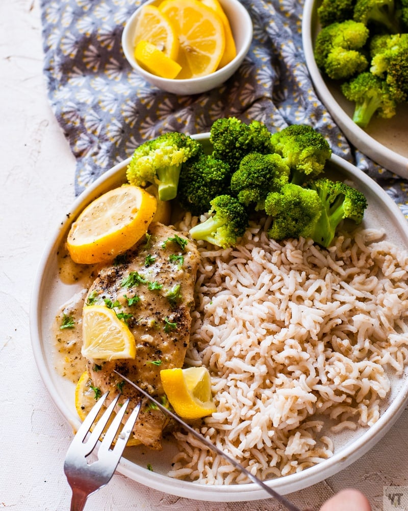 instant pot lemon garlic chicken on a white plate with a garnish of lemon slices and parsley on a bed of brown rice and steamed broccoli