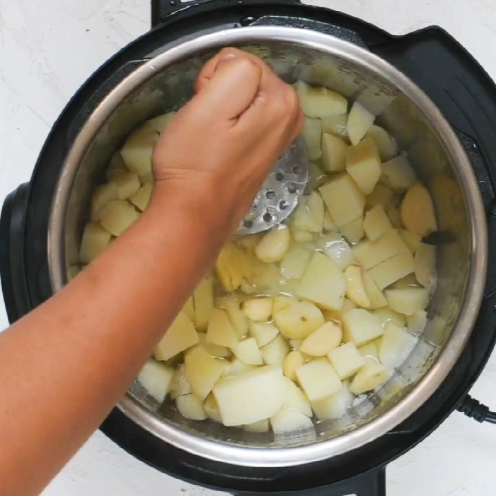 Mashing Pressure Cooked Potatoes, garlic and water to make no drain mashed potatoes in the instant pot, using the potato masher