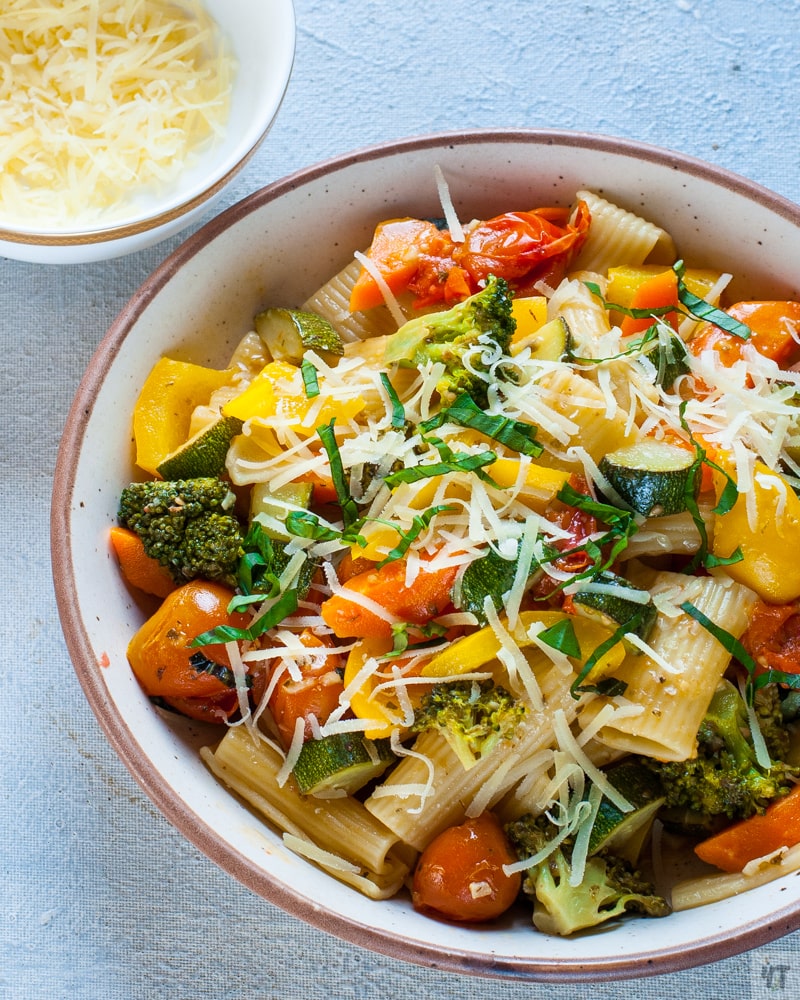 Pasta primavera with broccoli, tomatoes, zucchini, made in the instant pot, in a beige bowl, with grated cheese and strips of basil on top.