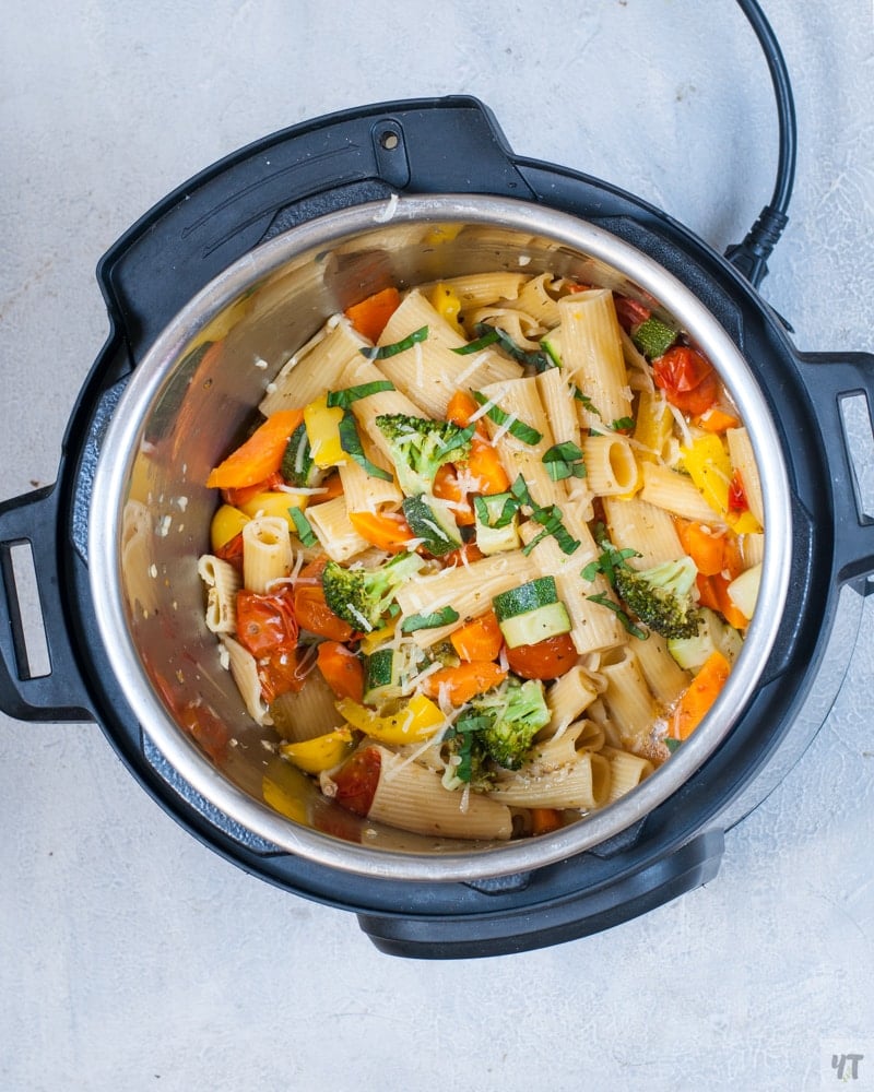 Instant Pot Pasta primavera with broccoli, tomatoes, zucchini,  in the instant pot, with grated parmesan cheese and strips of basil on top.