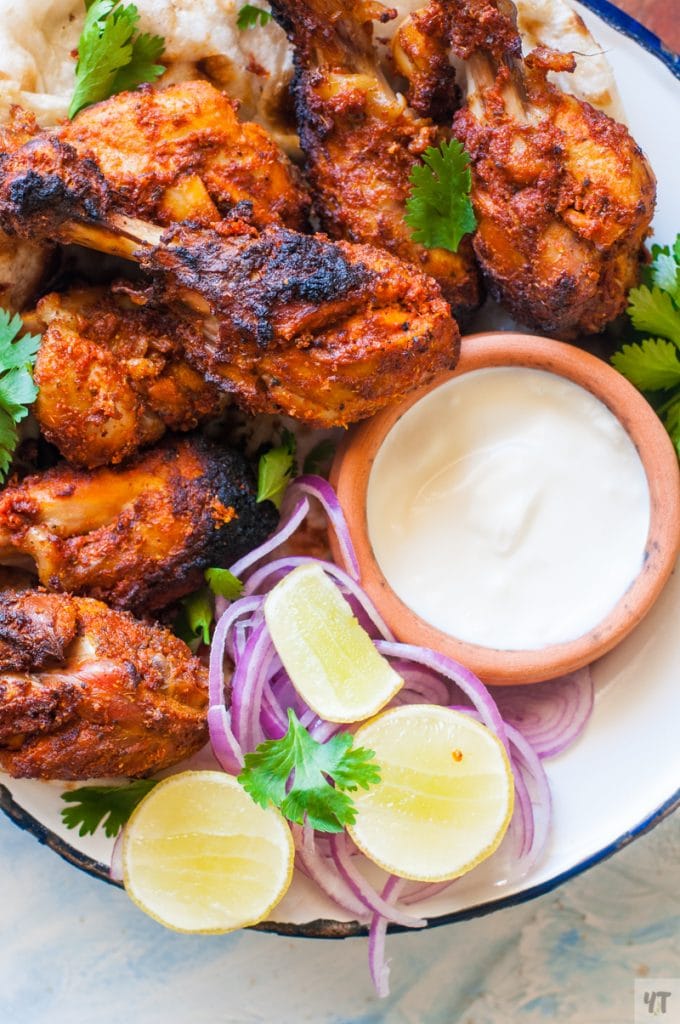 Tandoori Chicken drumsticks on a white plate with lime and onions