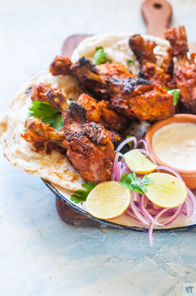 Tandoori Chicken drumsticks on a white plate with lime and onions