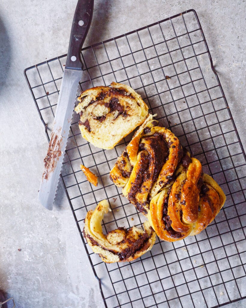 Chocolate babka on top of a cooling rack, cut into slices using a serrated knife
