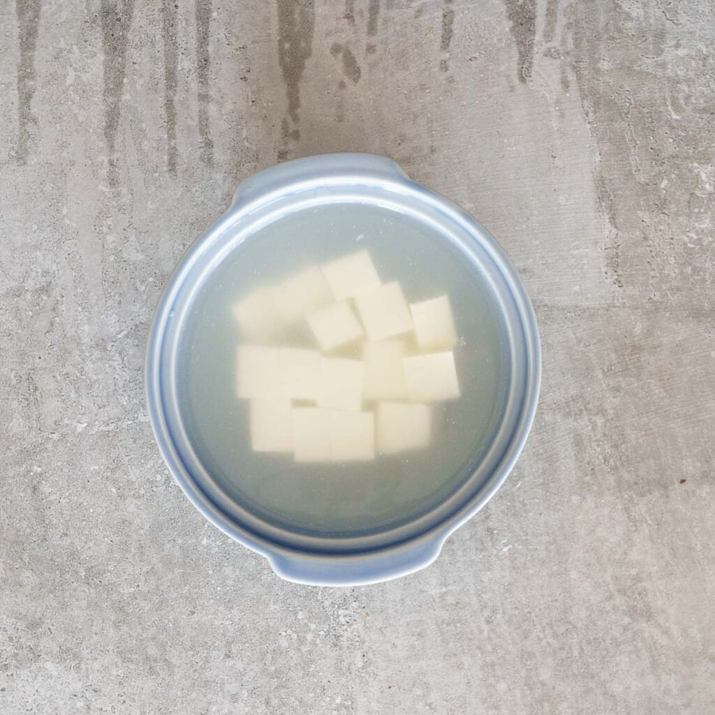 soaking paneer in warm water with vinegar in a blue bowl