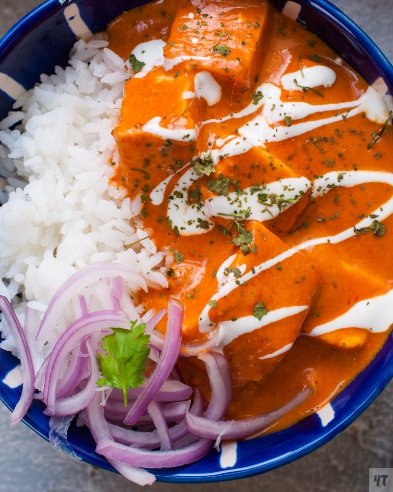 Paneer butter masala or paneer makhani in a blue bowl with rice and onions