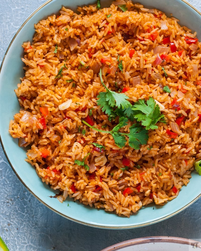 Red coloured rice with a sprig of coriander in a light green bowl