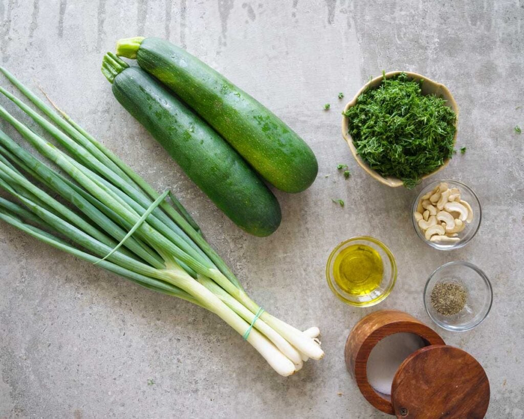 Ingredients needed to make Zucchini soup in the instant pot.You can see 2 zucchinis, cashew, dill, pepper, salt, olive oil and scallions