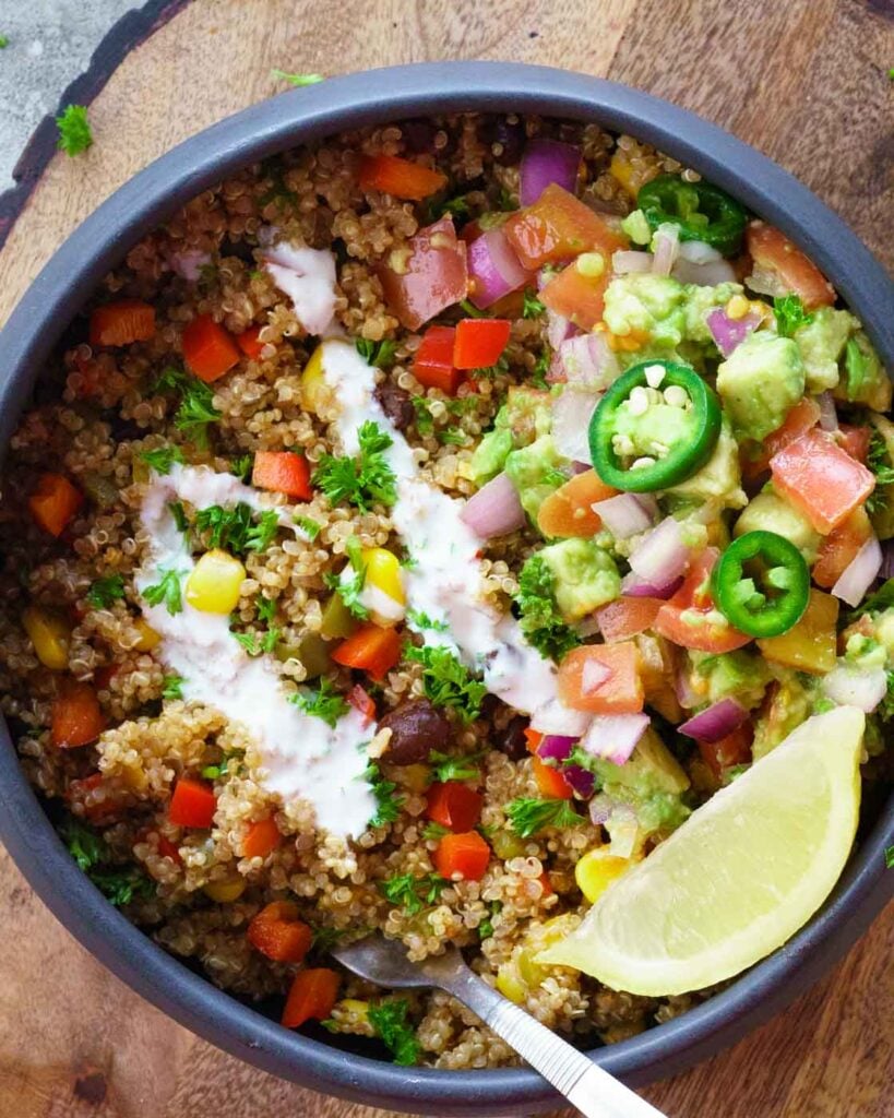 Instant Pot Mexican Quinoa Bowl with a lemon wedge, avocado salad in a black bowl