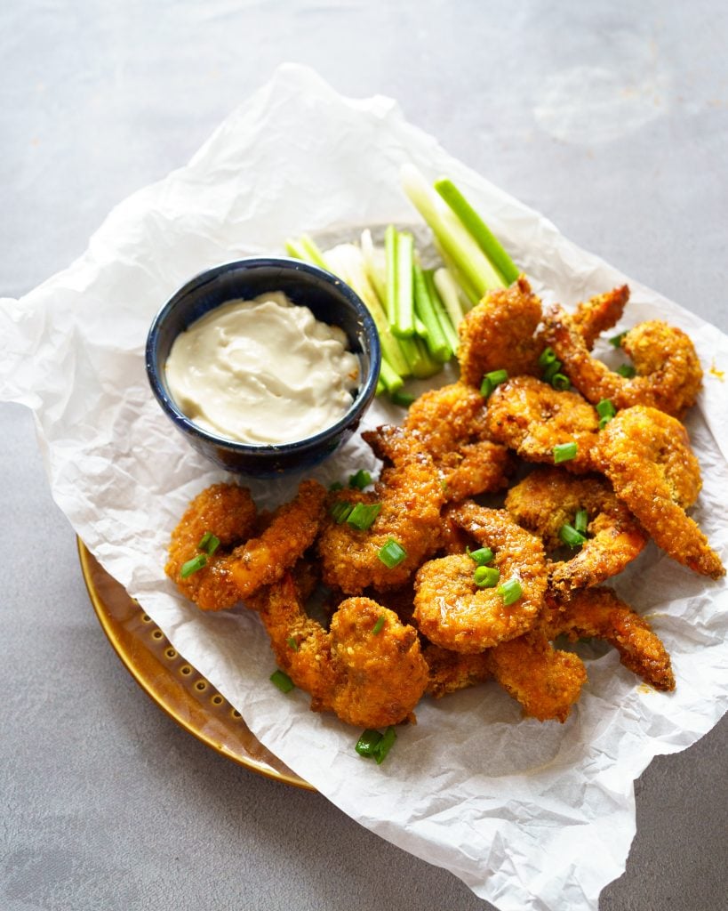 Air Fryer Buffalo Shrimp on a plate with parchment paper, celery and mayonnaise