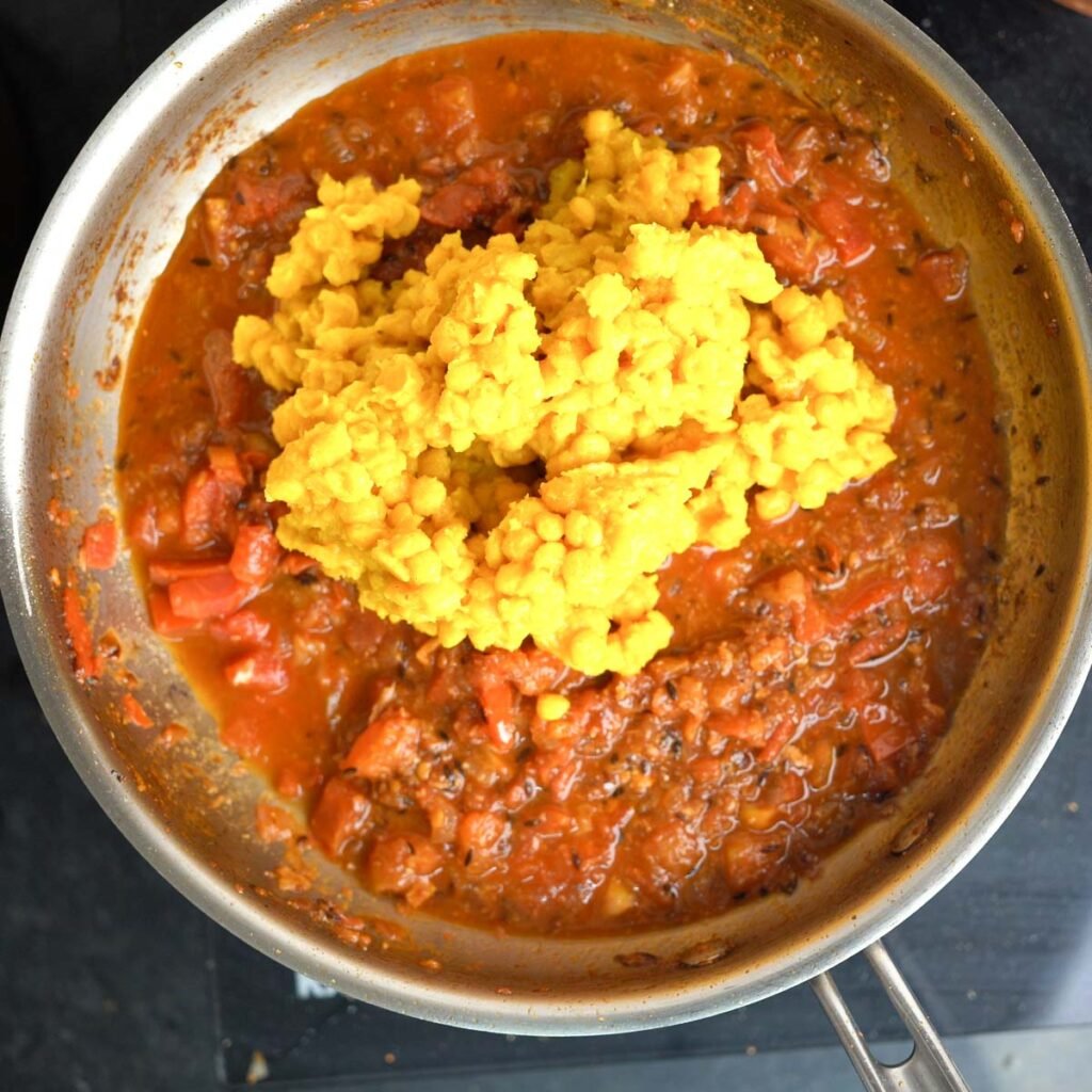 Adding Cooked chana dal to a pan of base sauce made with onions, tomatoes and spices.