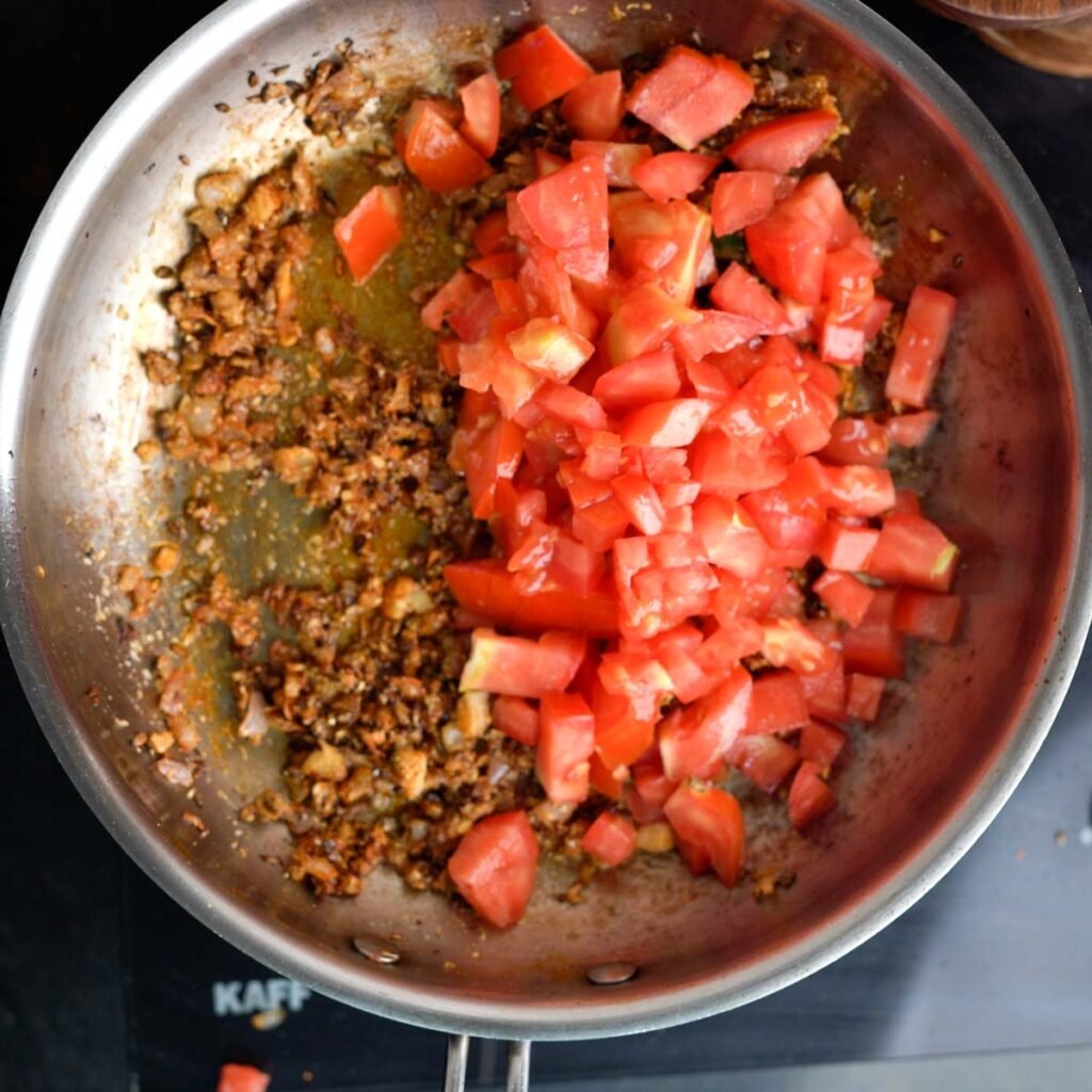 chopped Tomatoes inside a steel pan with brown onions and spices