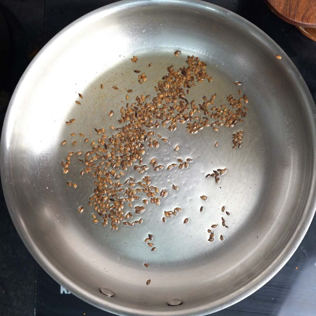 Adding cumin to a steel pan with ghee