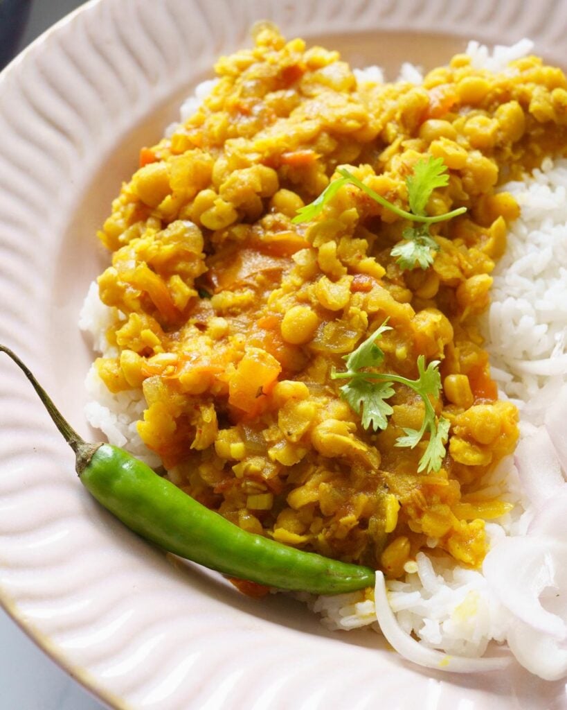 Close up of Chana Dal served on top of rice, in a pink bowl along with onions, chili and coriander