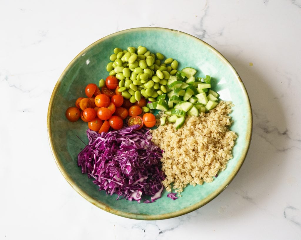 Quinoa, cucumber,edamame,tomatoes and purple cabbage in a green bowl to make Edamame Quinoa salad