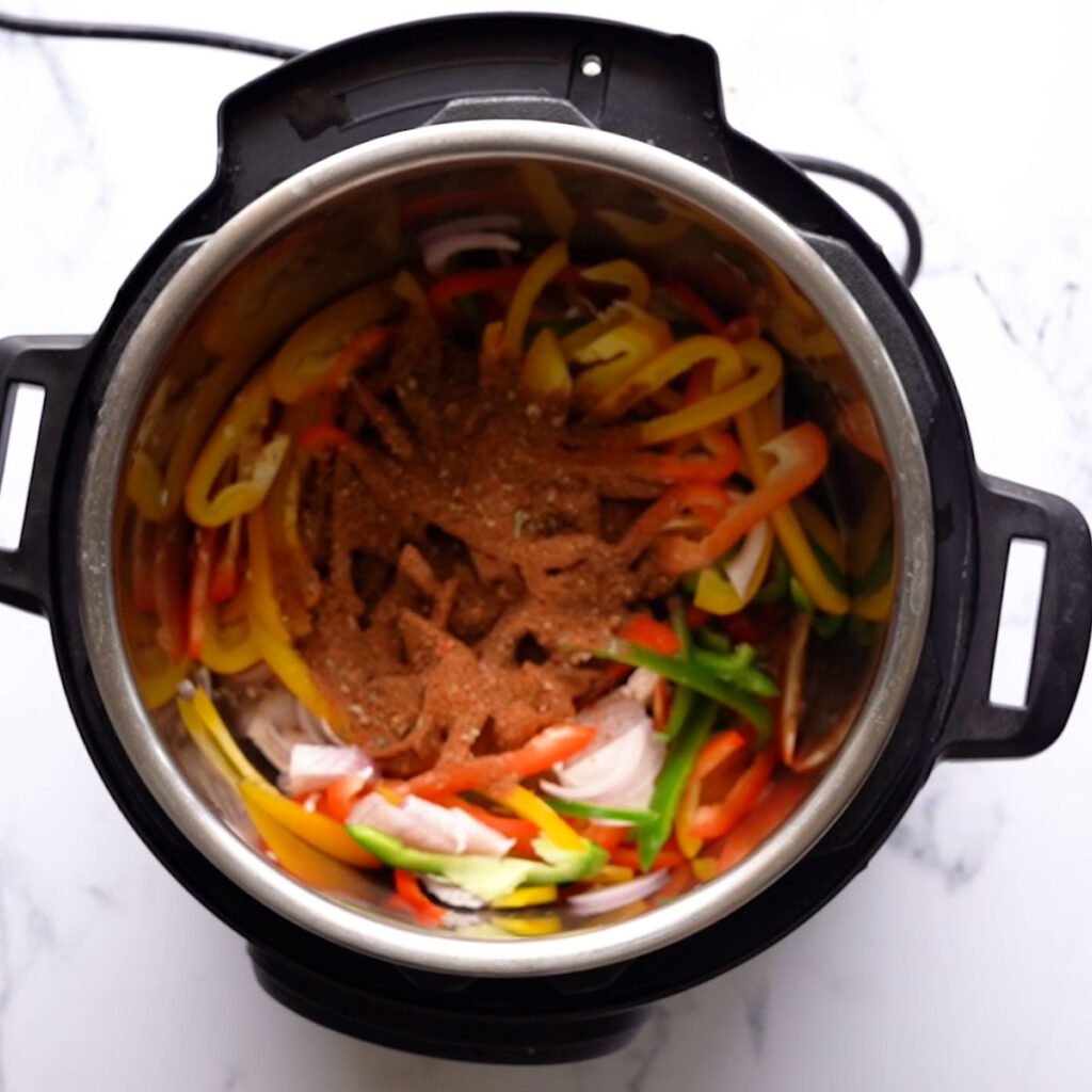 Sliced chicken in the instant pot along with bell peppers, taco seasoning and onions