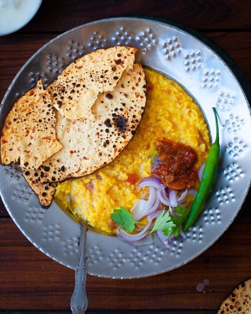 Instant Pot Moong Dal Khichdi(Kichdi /kitchari) in a steel plate with pickle, papapd, onions and a chili