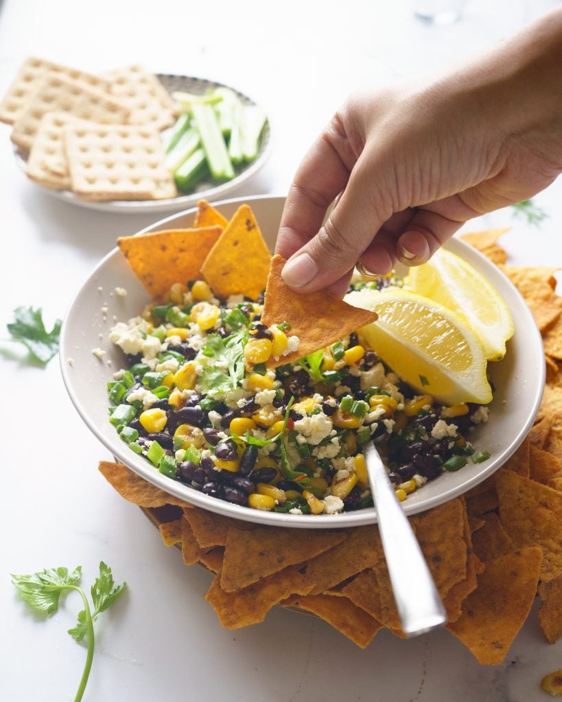 Black bean corn and feta dip in a grey bowl served on a plate with chips