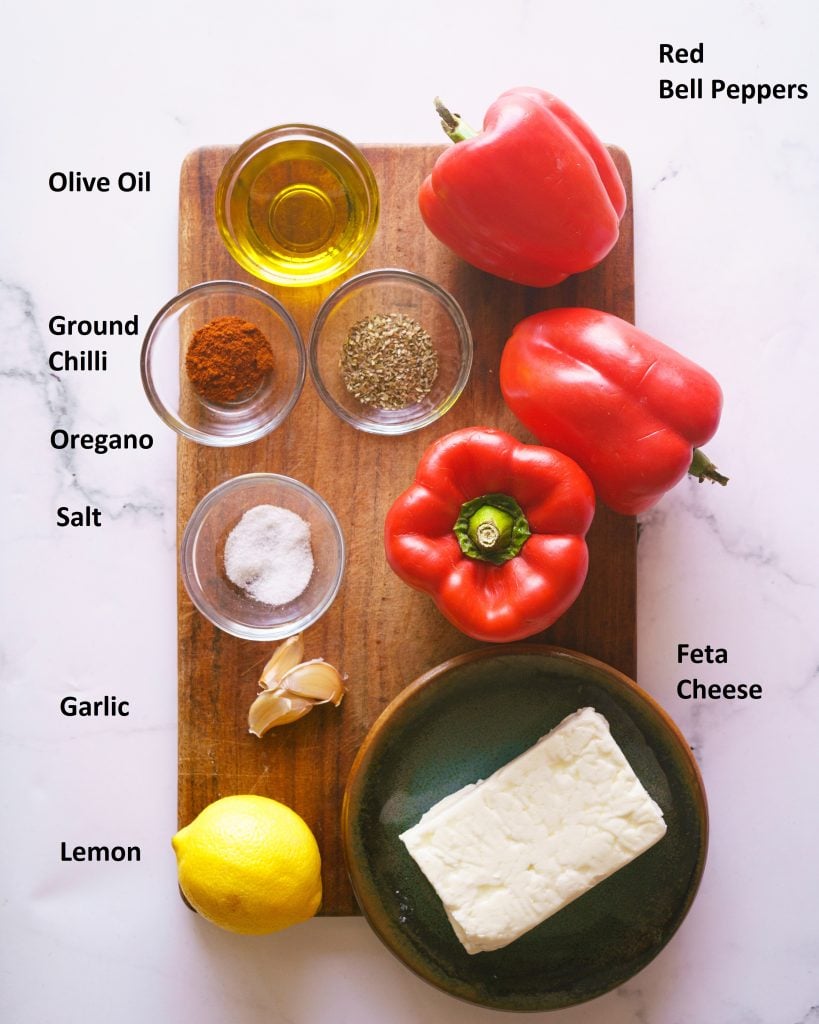 ingredients needed to make the pepper feta dip- Red peppers, feta cheese, lemon, salt, oregano, ground chilli, olive oil, salt on a brown platter