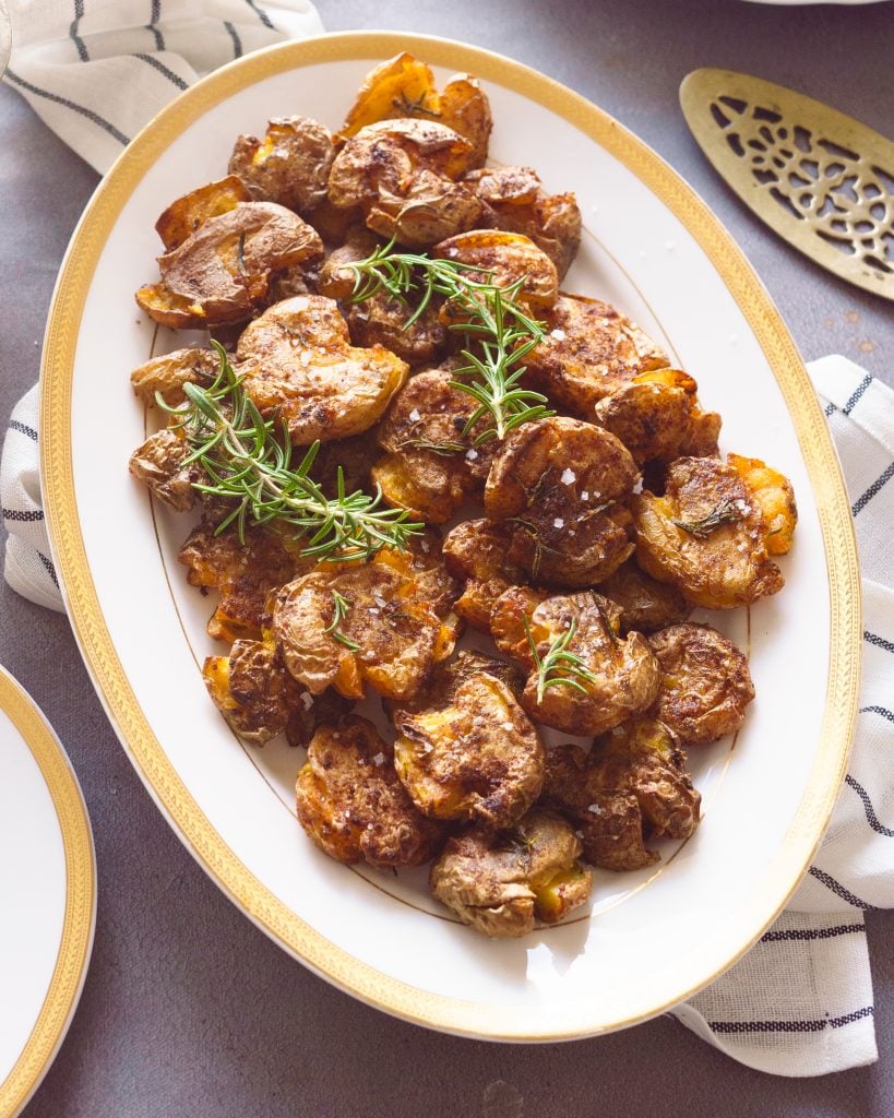 air fryer smashed potatoes in a oval white platter with rosemary and sea salt